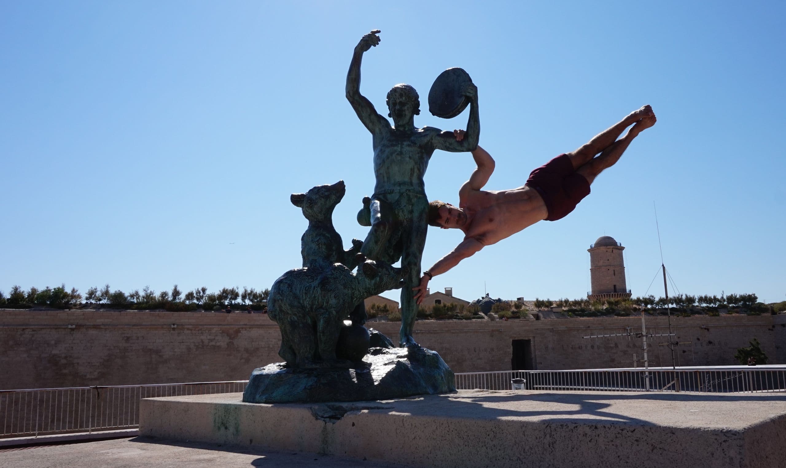 Nikjas Sakowski hält sich waagerecht an einer Bronzestatue auf einer Festungsmauer