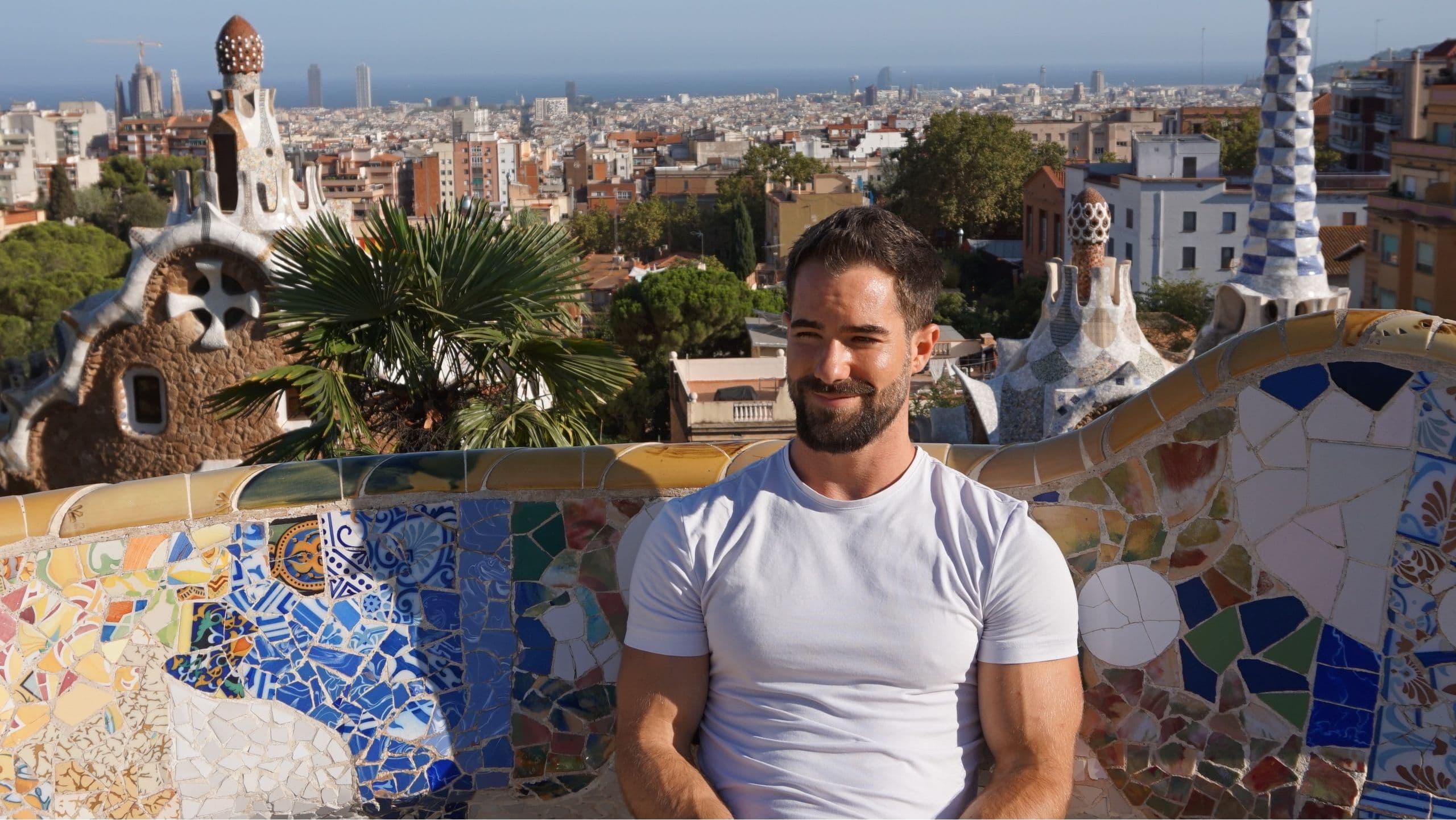 Nikjas Sakowski sitzt auf der Mosaikbank im Park Güell, dahinter Barcelona